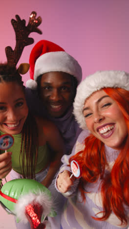 Vertikale-Videostudioaufnahme-Von-Freunden-Der-Generation-Z,-Die-Auf-Der-Weihnachtsfeier-Mit-Weihnachtsmütze-Und-Rentiergeweih-Tanzen-Und-Für-Ein-Selfie-Posieren-1